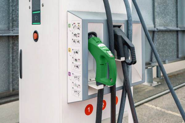 A close view of a commercial charging station with its green connector resting in the holster, built to take heavy daily use at a business.